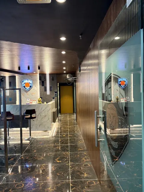 Corridor from the glass entrance towards the reception, with a wood-panelled wall and gold-veined black floor