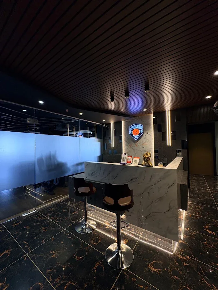 Marble-finish reception desk with bar stools and the illuminated Jaguar Fitness Den shield on the wall
